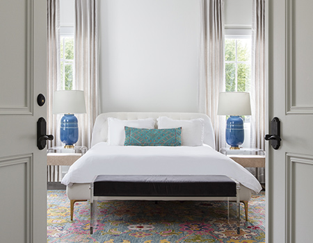 Large french doors leading into a guest room with king sized bed between two large windows with floor to ceiling curtains in Houston, TX